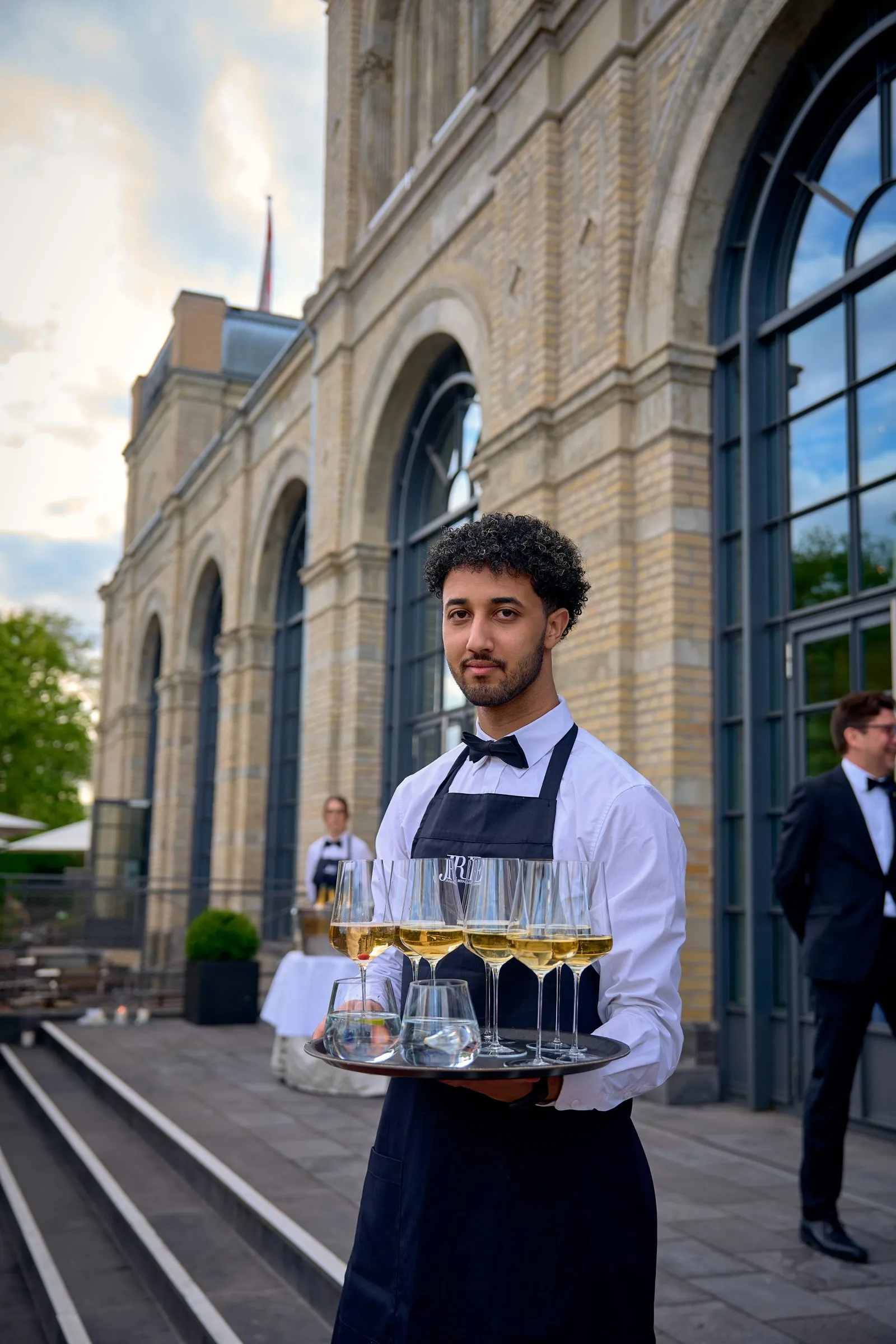 Kellner mit Tablett vor dem Gebäude